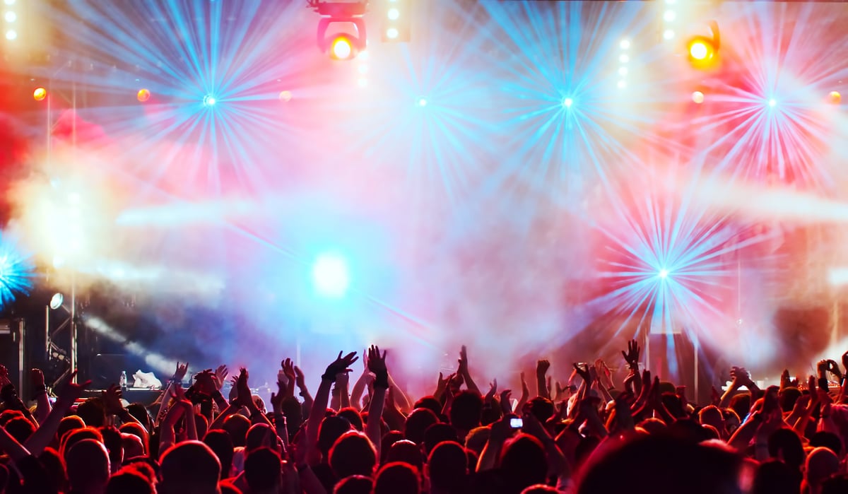 Crowd with raised hands at a concert with vibrant stage lights